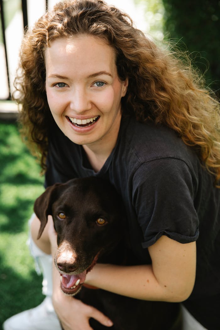 Content female with curly hair embracing pointing dog with open mouth while looking at camera in sunlight